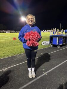Induction Innovations Interviewee Sadie Cheerleading at a Football Game with Pink Pom Poms for Breast Cancer Awareness